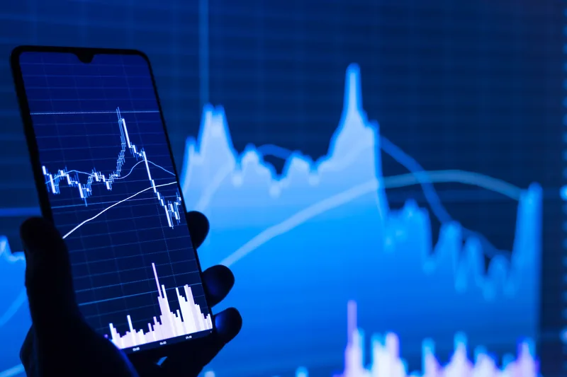 Smartphone showing a stock chart against a blue financial graph