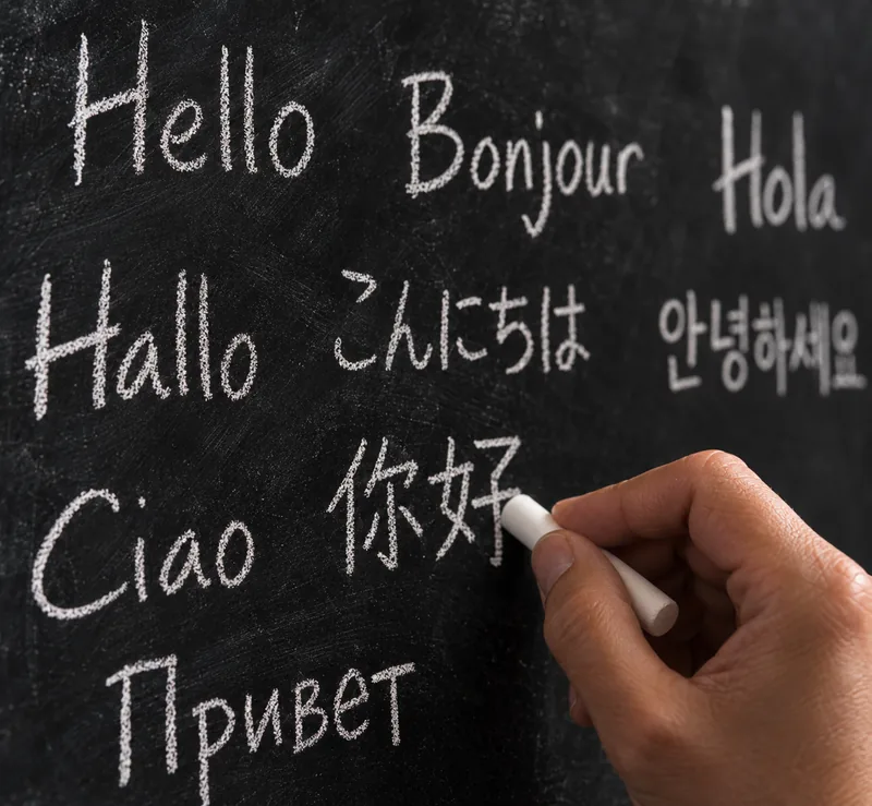 Hand writing greetings in several languages on a chalkboard