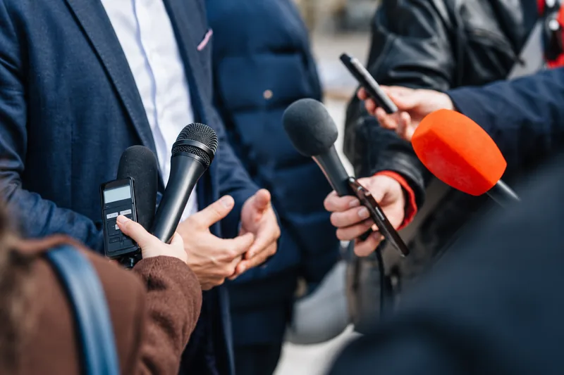 Reporters holding out microphones to a speaker