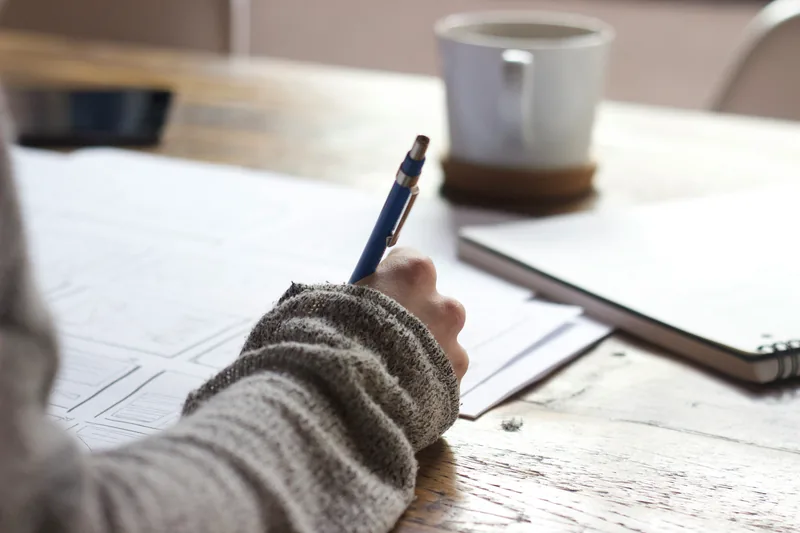 Student writing notes by hand at a desk beside a cup of coffee