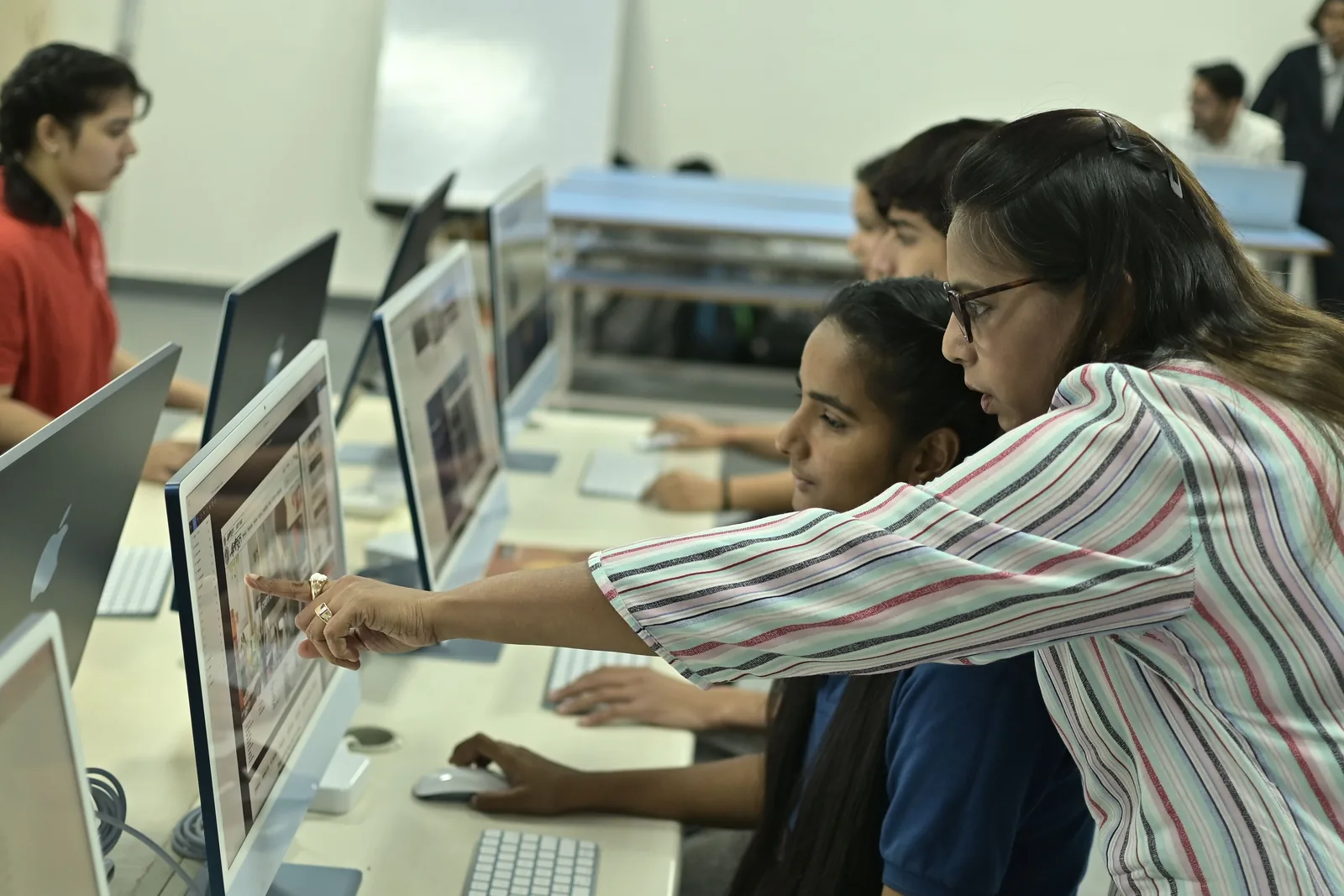 An instructor leaning in to help a learner at a row of computers