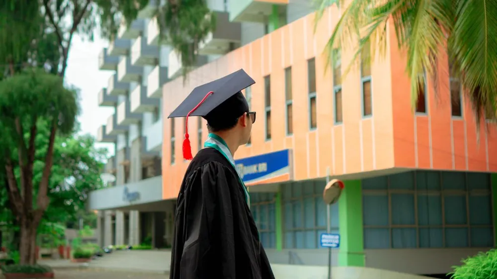 A graduate in cap and gown looking up at a college building